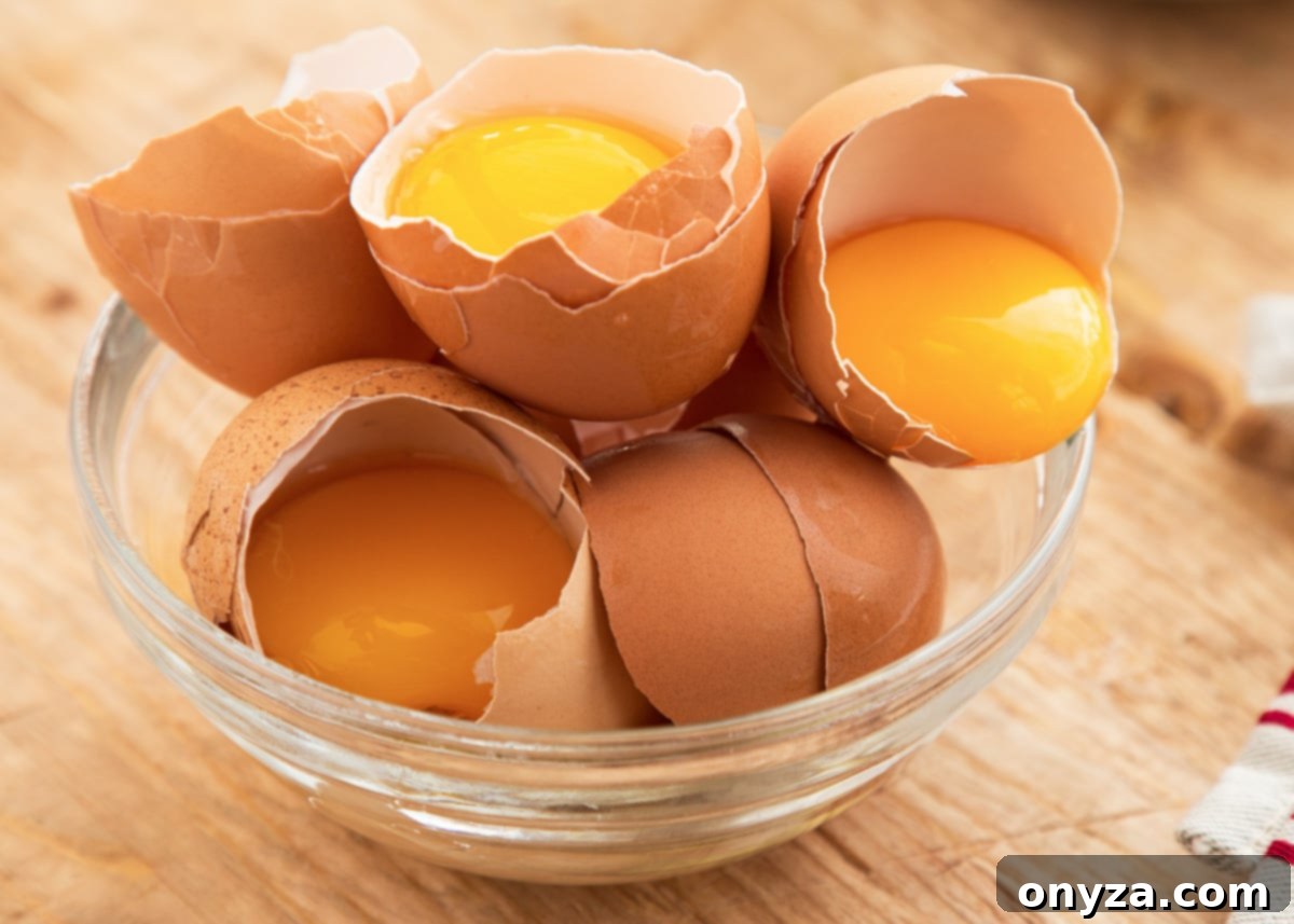 Close-up of golden egg yolks in a clear glass bowl, nestled within their broken brown eggshells, highlighting a key ingredient for the soufflé.