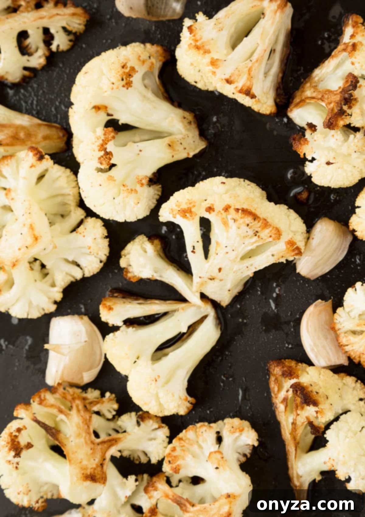Close-up of beautifully roasted cauliflower florets, golden and caramelized, spread out on a black sheet pan.