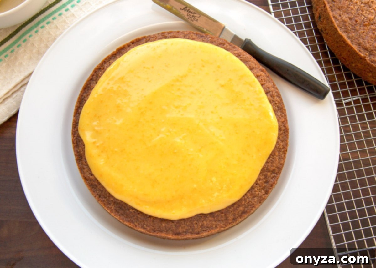 The base layer of carrot cake beautifully spread with a vibrant orange curd filling, demonstrating the first step of cake assembly.