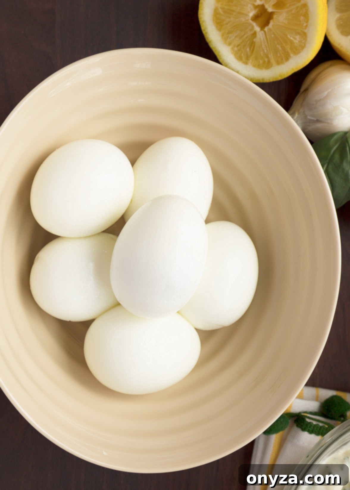 Six perfectly hard-boiled eggs resting in an ivory ceramic bowl, ready to be prepared for basil egg salad. Overhead view.