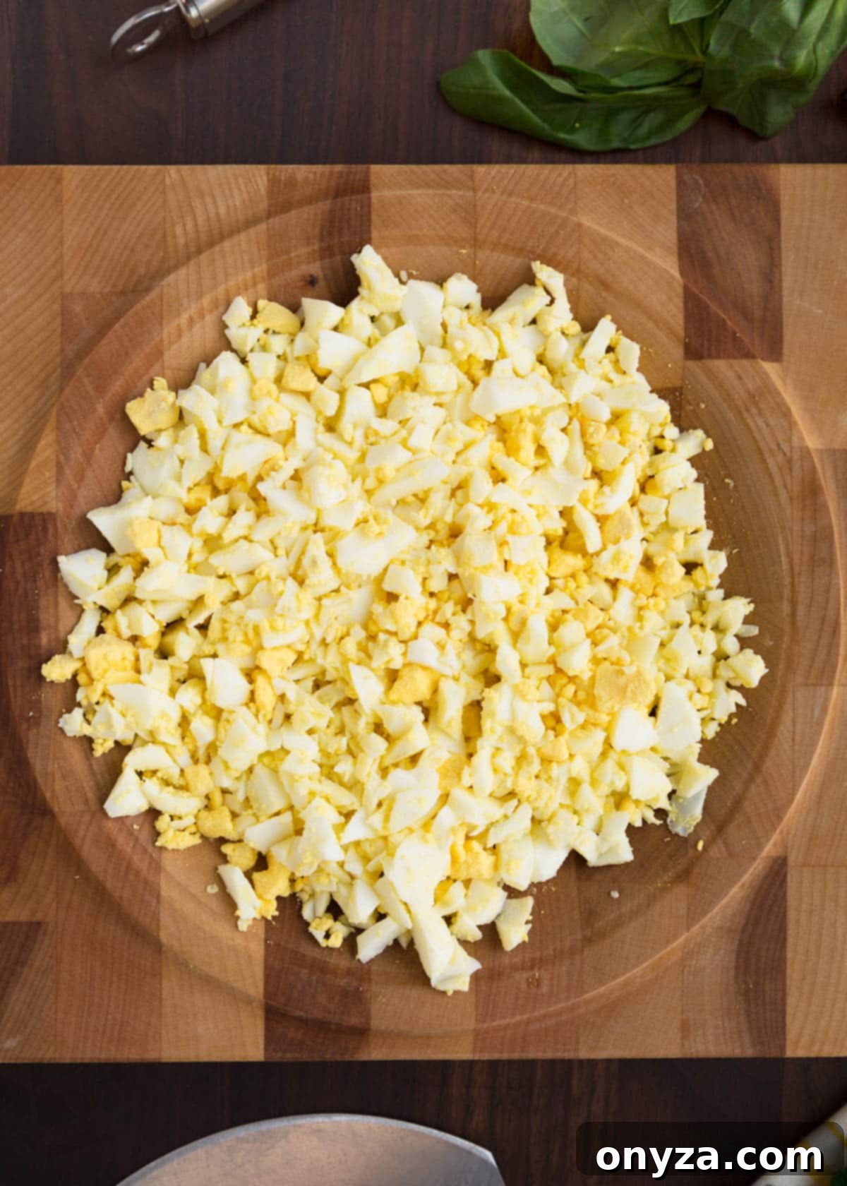 Chopped hard-boiled eggs in a wooden mincing board, prepared for mixing into the basil egg salad dressing. Overhead view.