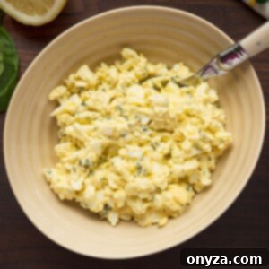 A vibrant Basil Egg Salad in a bowl next to a sandwich, showcasing its deliciousness.