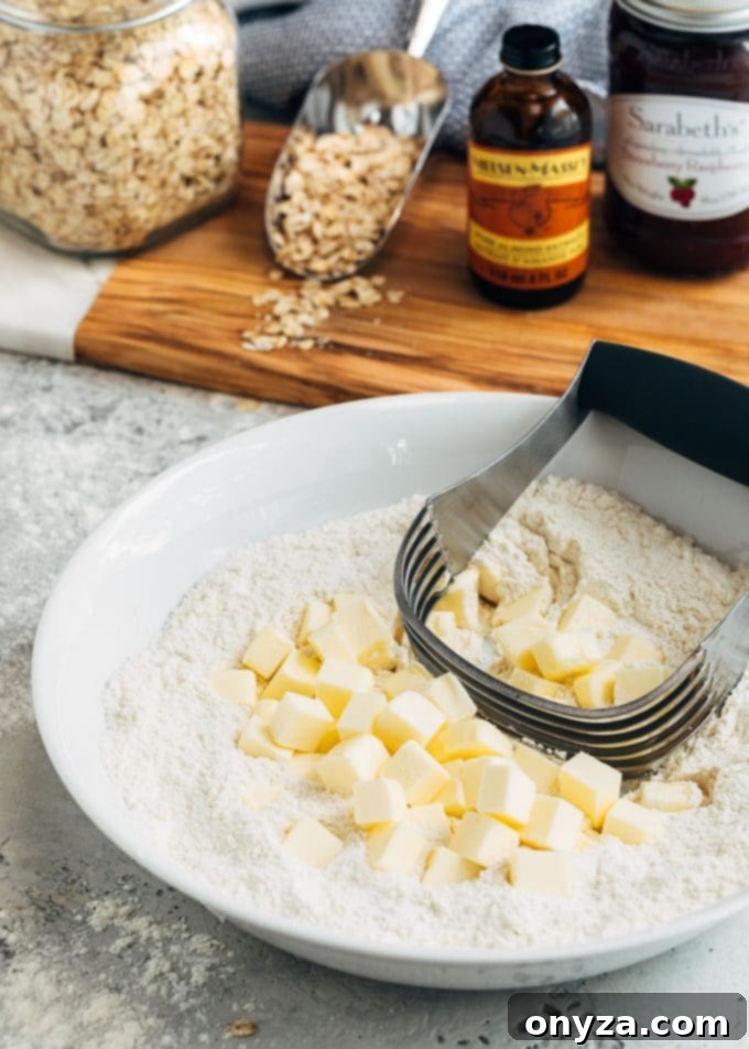 Close-up of butter cubes, flour, and a pastry blender in a mixing bowl, preparing the crust for jam bars.