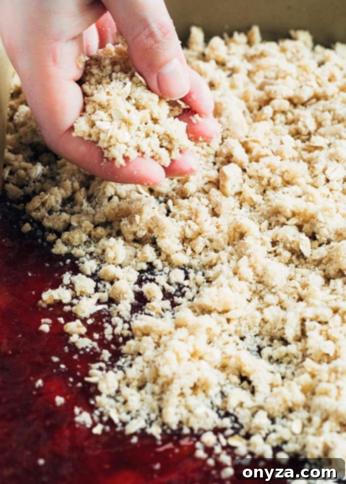 Someone sprinkling oat crumble topping evenly over a layer of jam on a pre-baked crust