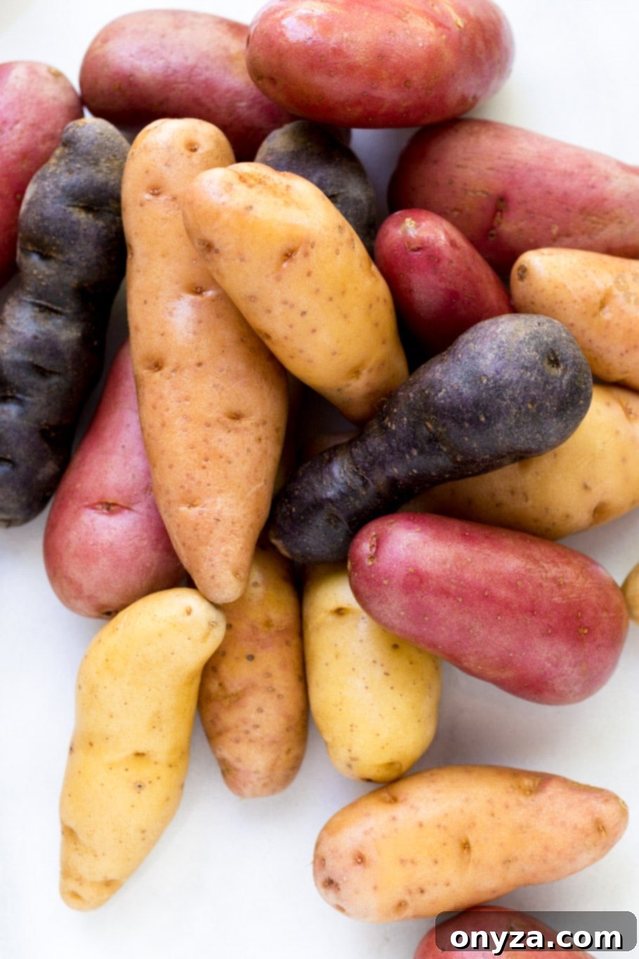 A colorful assortment of red, purple, and white fingerling potatoes displayed on a white marble board, ready for preparation.
