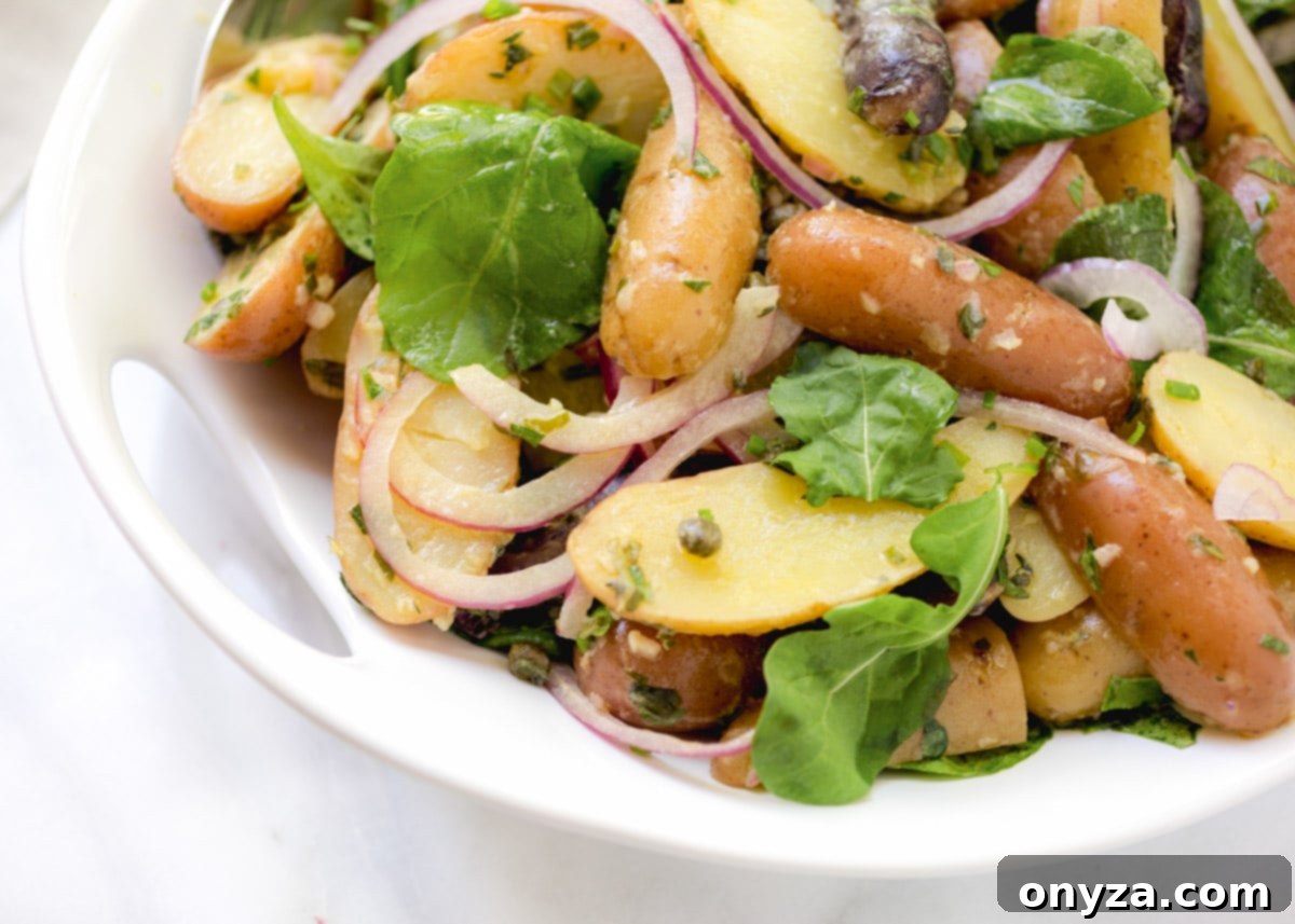 Close-up of vibrant fingerling potato salad with visible red onions and baby arugula, artfully arranged in a white serving bowl.
