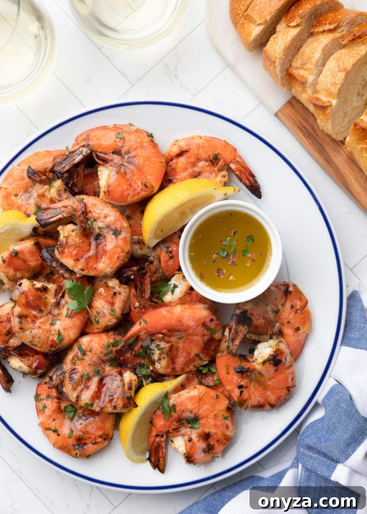 Grilled lemon garlic shrimp on a blue rimmed white plate with lemon wedges and a bowl of dipping butter, showcasing perfectly charred shrimp