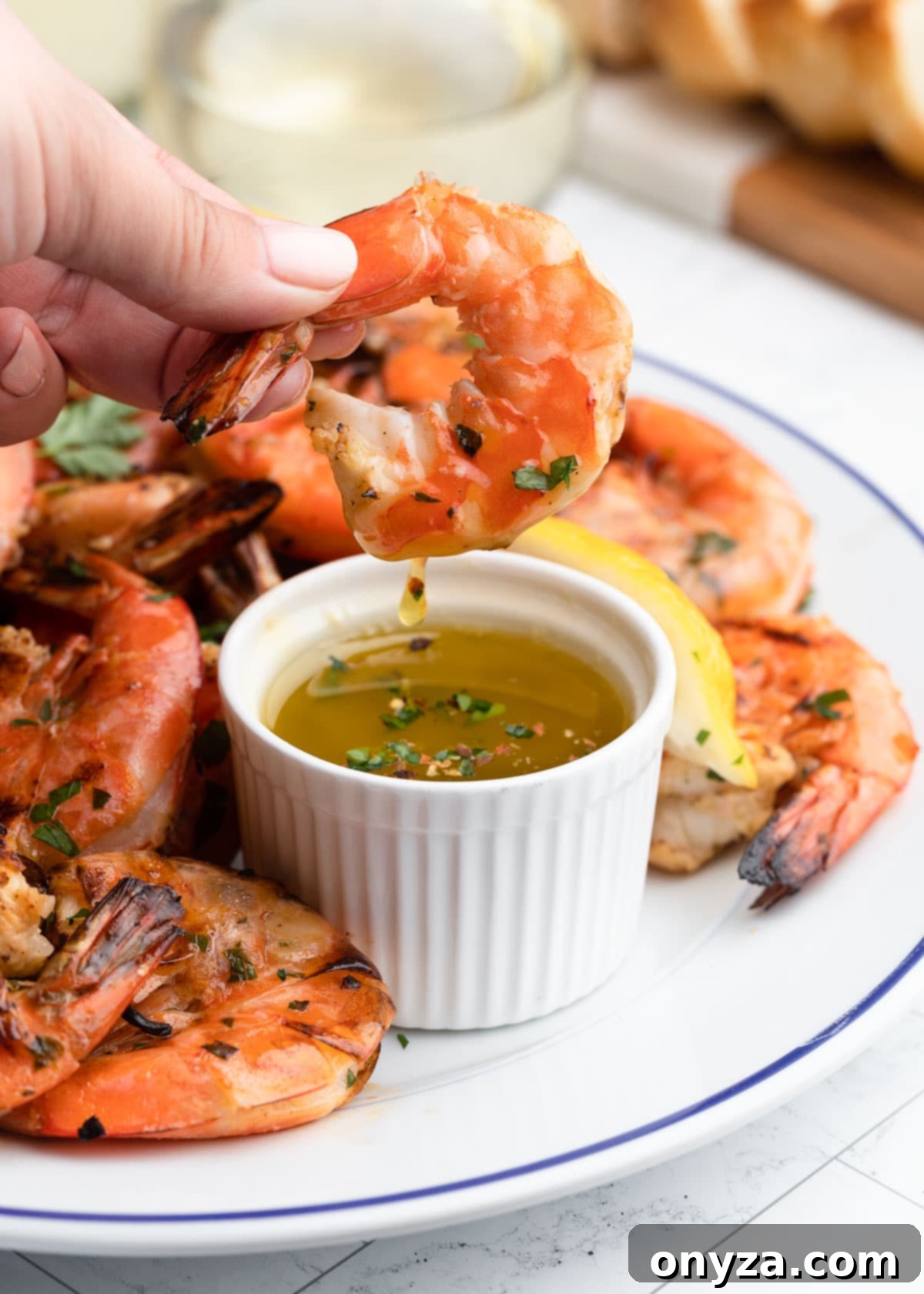 Shelled grilled shrimp being dipped into a bowl of warm lemon garlic butter, emphasizing the delicious serving method