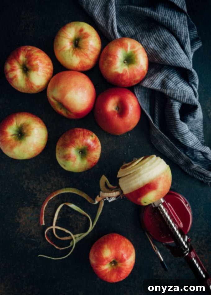 fresh apples arranged on a dark wooden board with an apple peeler tool