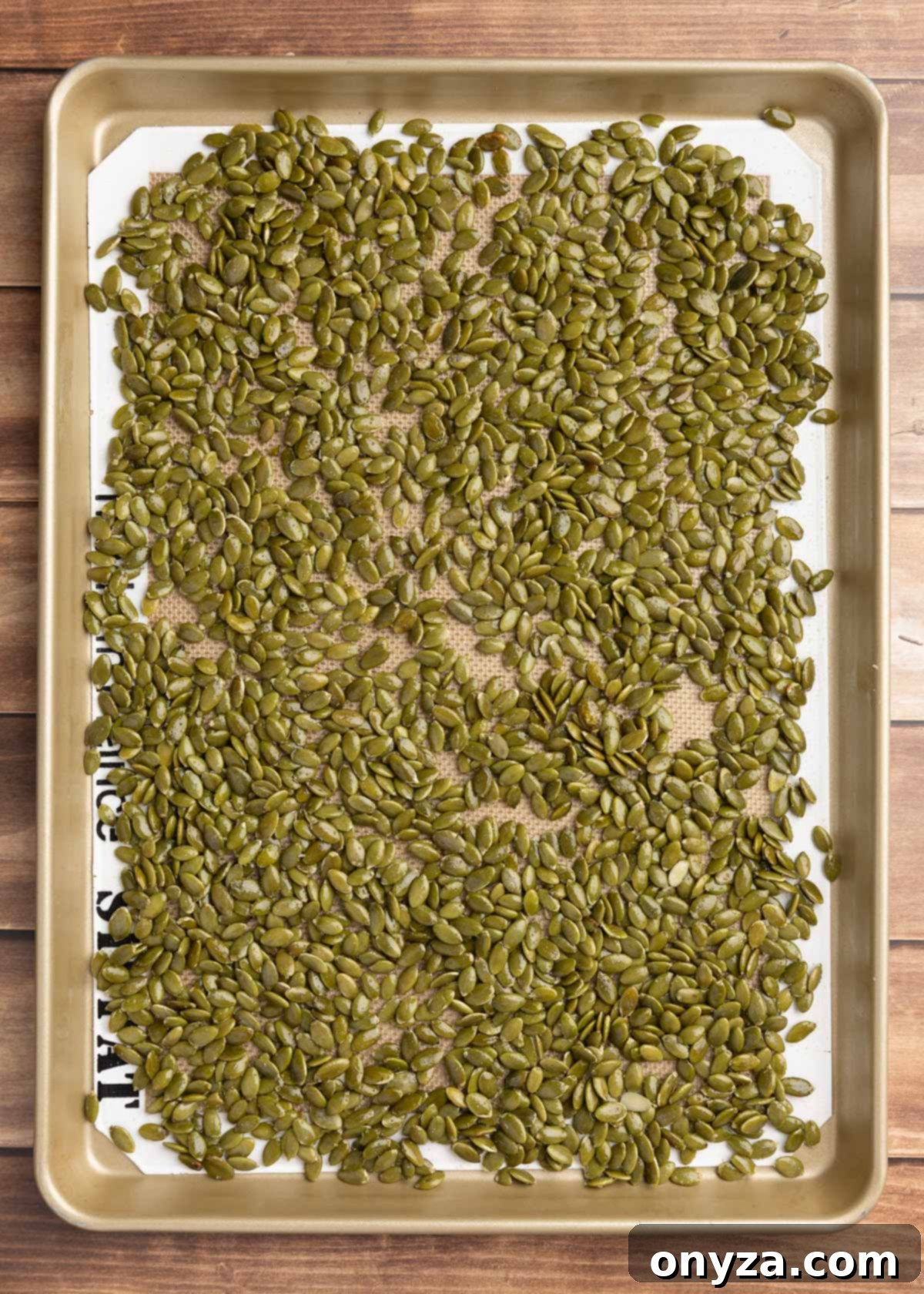 Raw pepitas, tossed with olive oil and salt, spread in a single, even layer on a silicone-lined baking sheet.