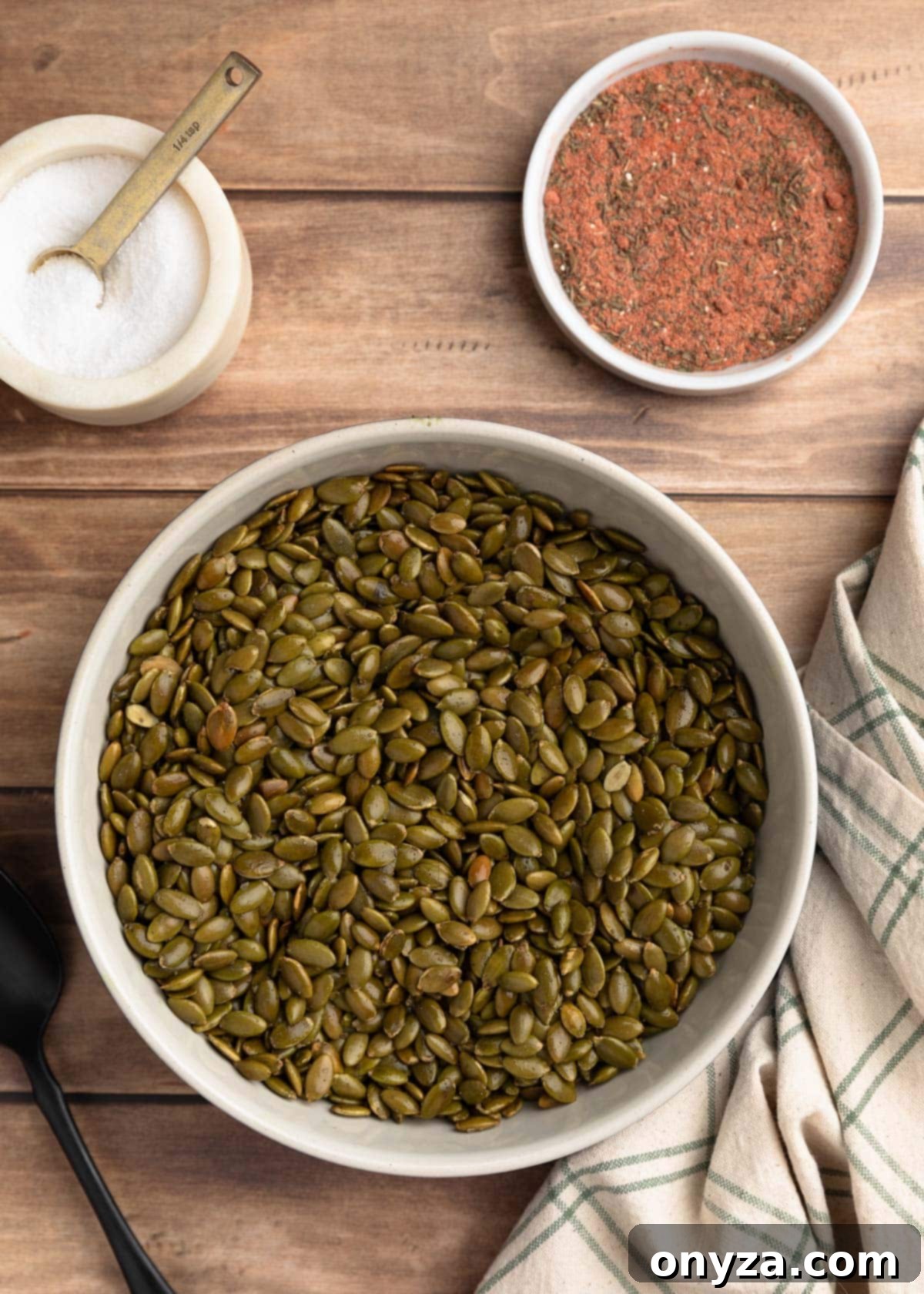 A ceramic bowl filled with freshly toasted pepitas, alongside a crock of salt and a small dish of the ground spice blend.
