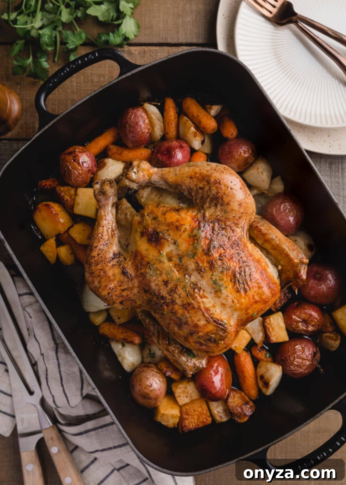 overhead photo of a roasted chicken with root vegetables in a cast iron roasting pan, golden brown and perfectly cooked