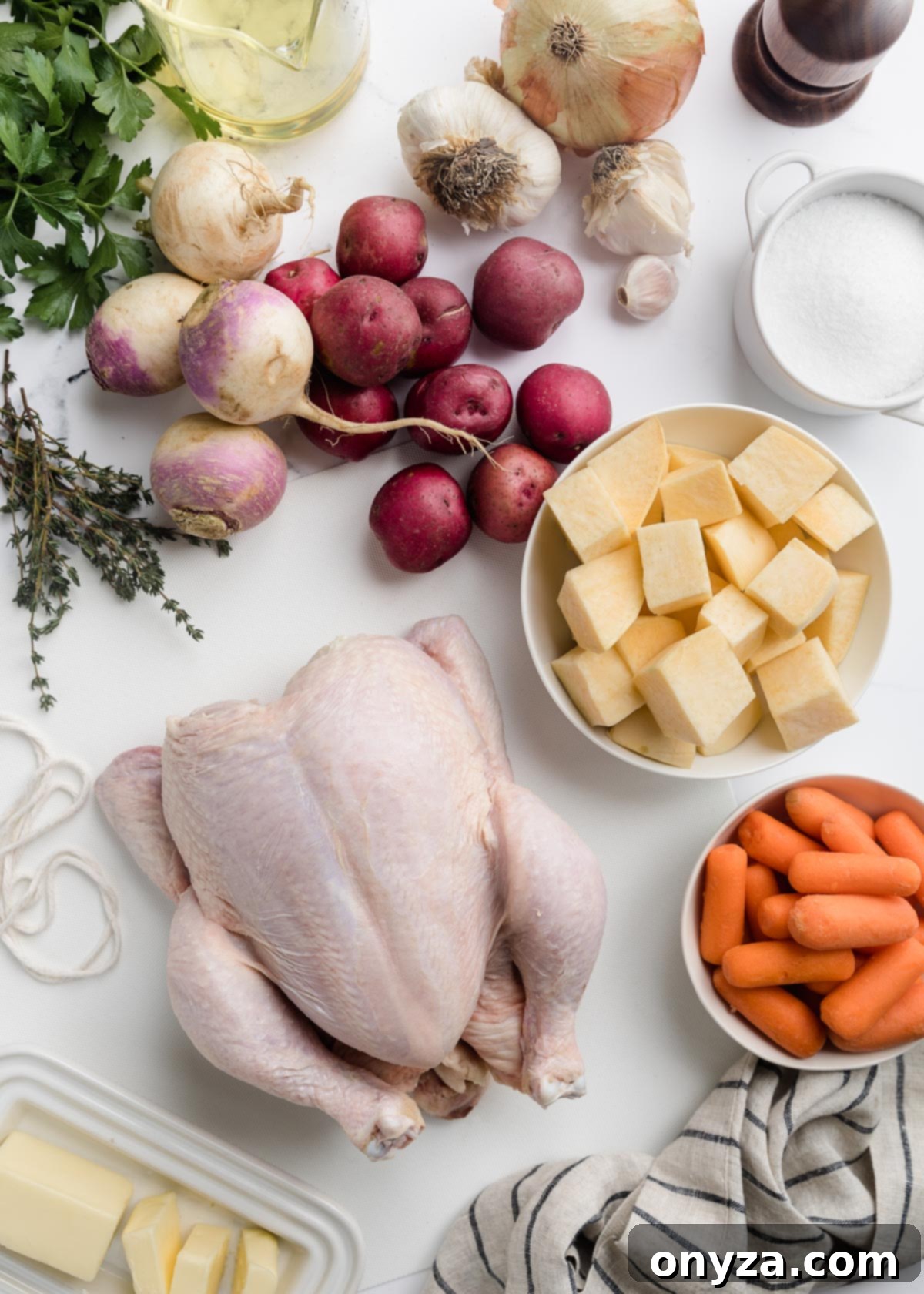 raw chicken and assorted root vegetables, fresh herbs, and seasonings laid out on a marble board