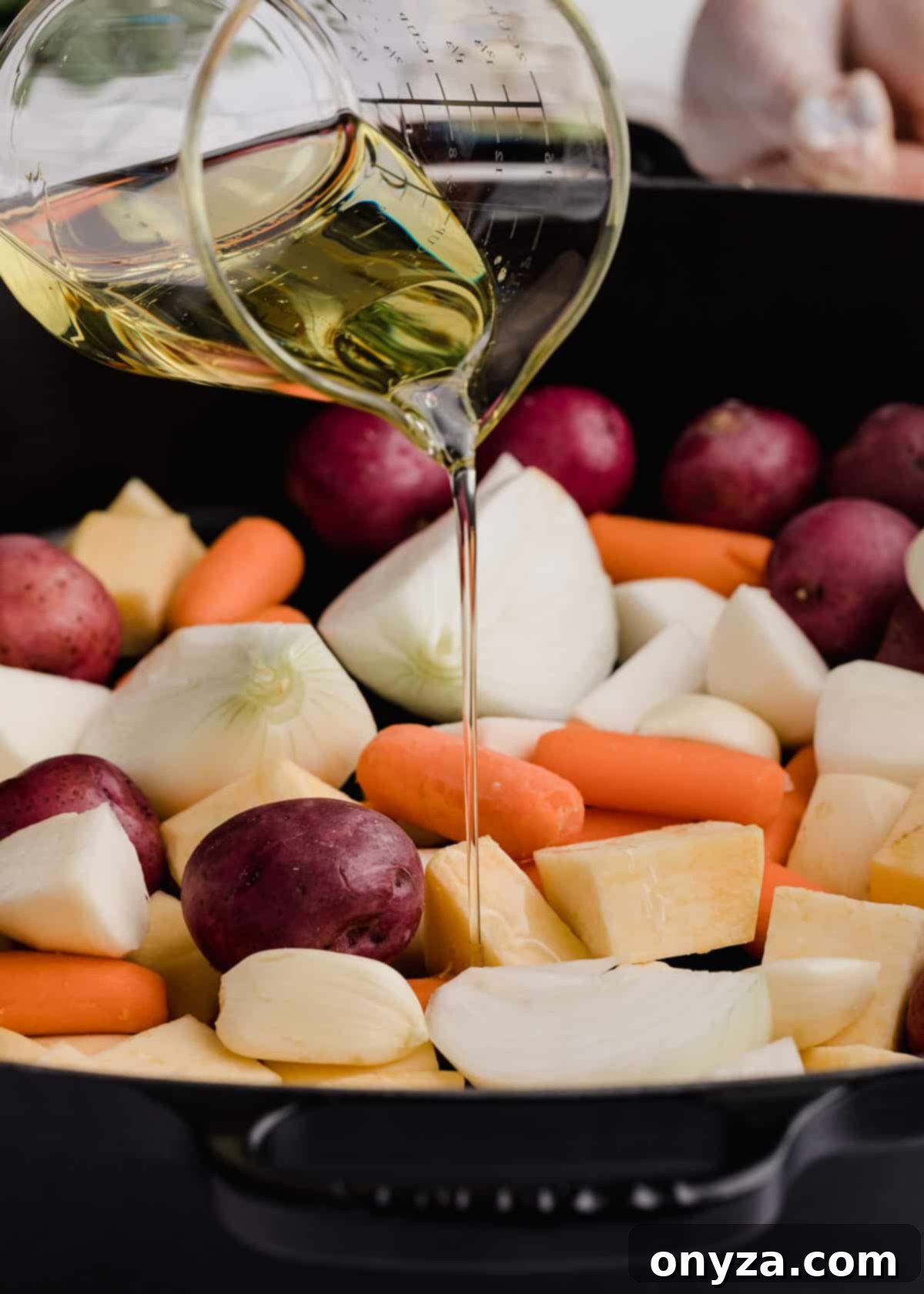 root vegetables in a cast iron roasting pan being drizzled with vegetable oil and fresh thyme