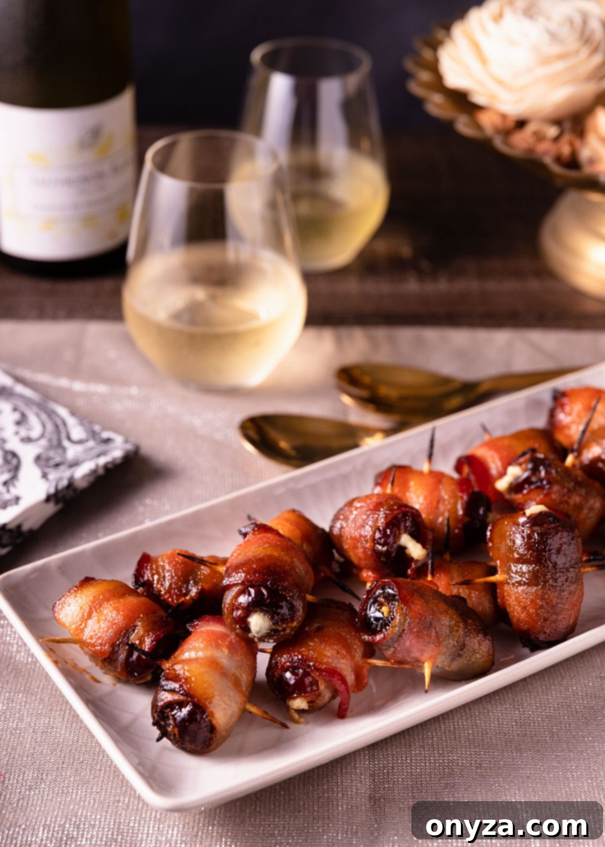 Maple Sriracha Devils on Horseback arranged on a white serving platter, complemented by napkins and glasses of wine