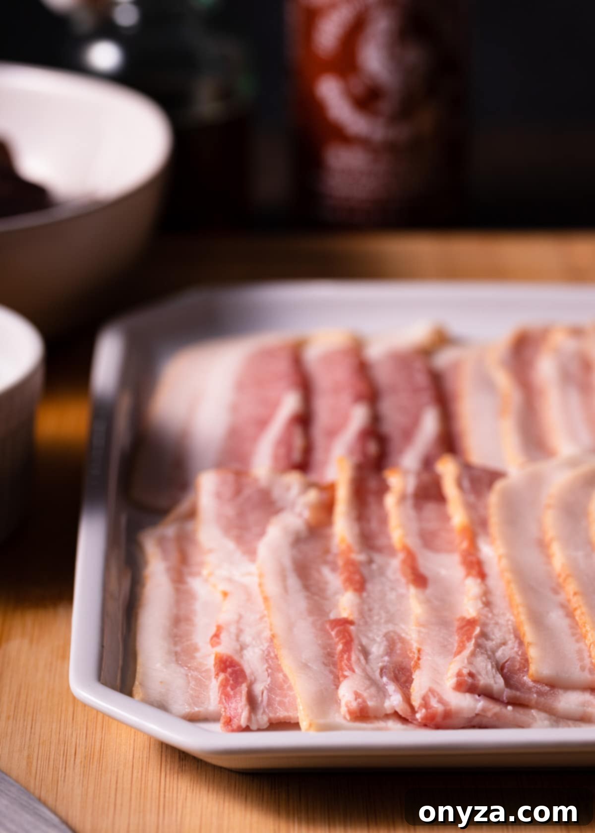 Strips of raw bacon are neatly arranged on a pristine white platter, awaiting preparation for the Devils on Horseback recipe.