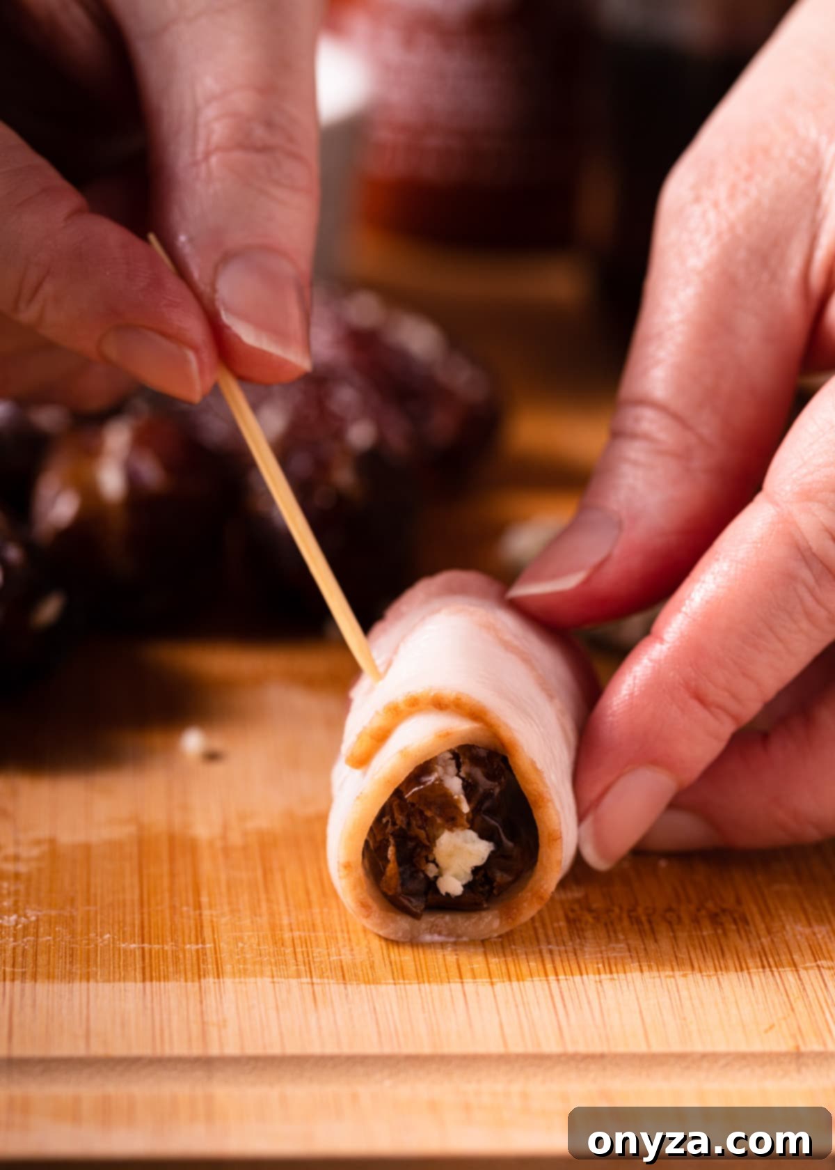 A bacon-wrapped date is being skewered closed with a pre-soaked toothpick, securing the bacon tightly around the date.