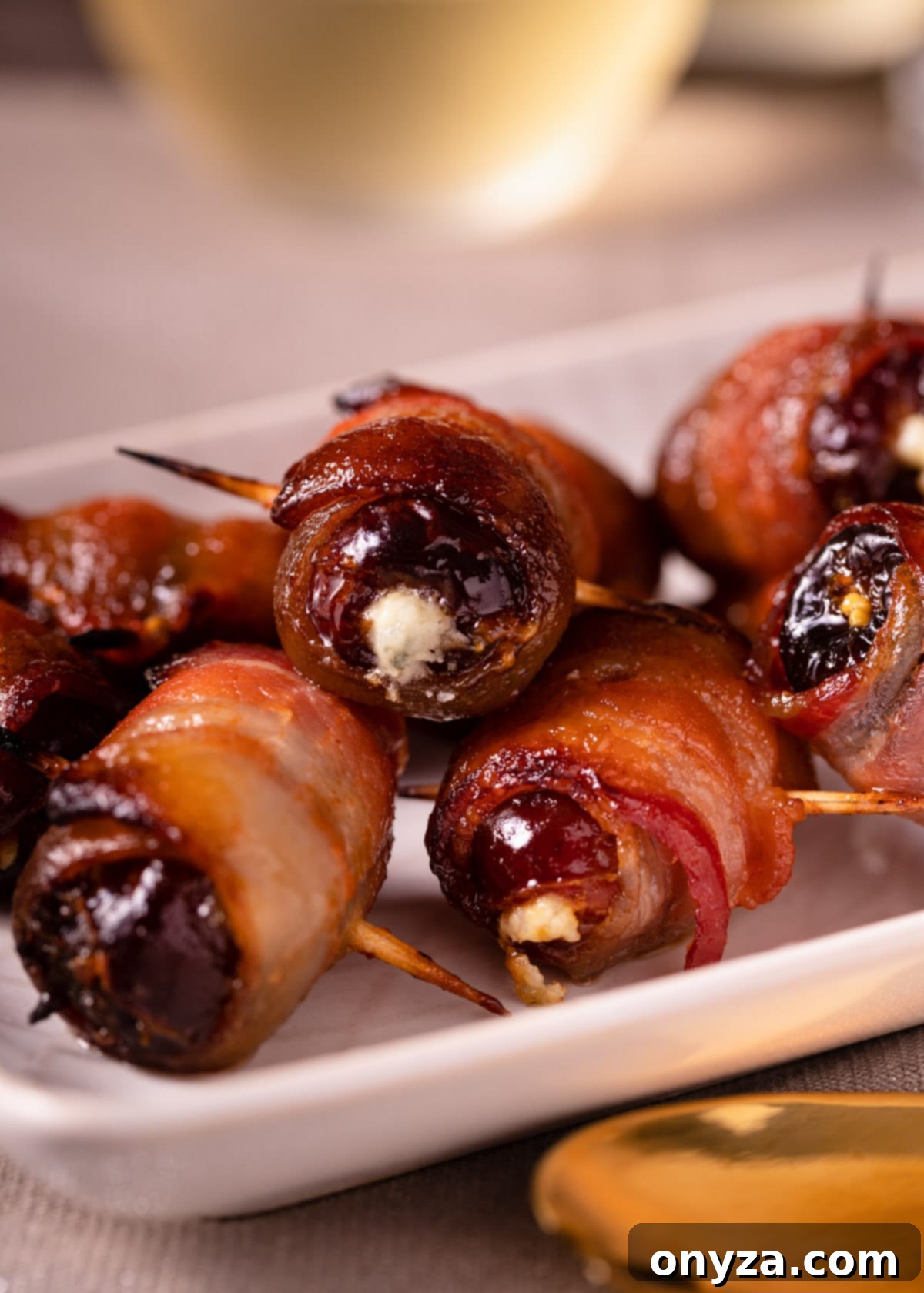 A close-up shot of several Maple Sriracha Devils on Horseback elegantly arranged on a white serving platter, showcasing their crispy bacon and glistening glaze.