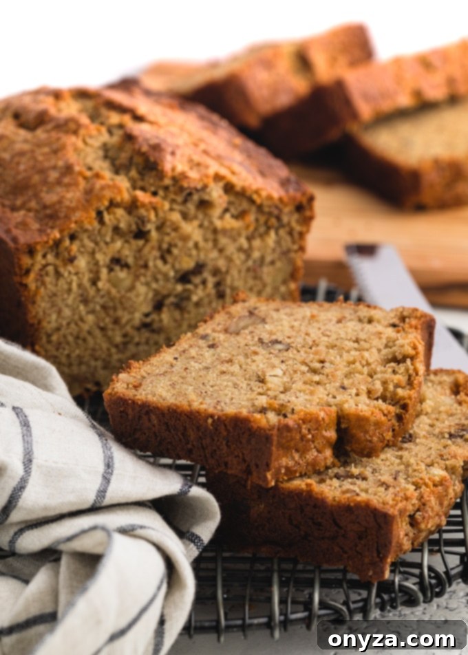 Slices of moist sour cream banana bread with brown butter on a black wire cooling rack, showcasing its golden-brown crust and tender crumb.