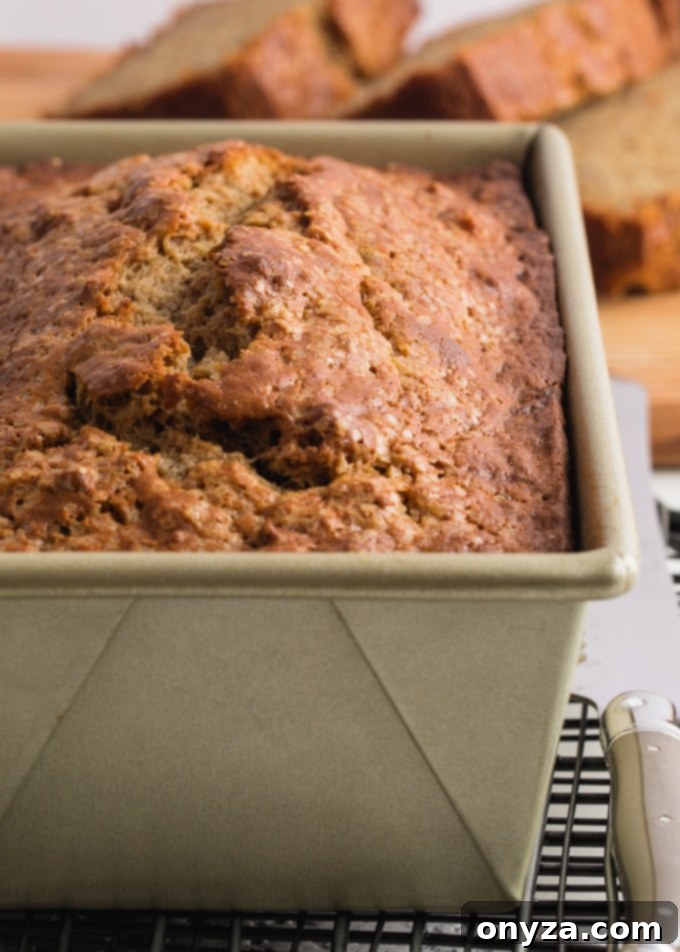 A perfectly baked loaf of brown butter sour cream banana bread cooling in a loaf pan on a wire rack.