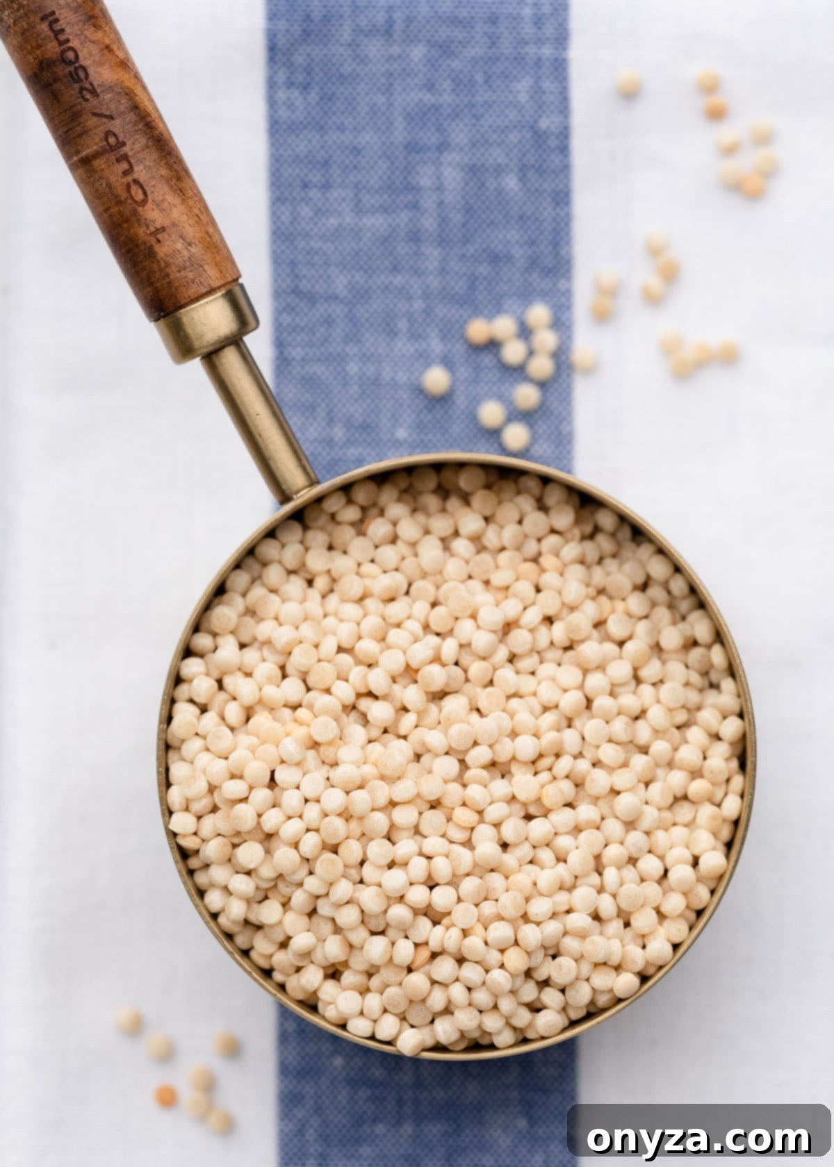 Flaked Salmon Couscous Salad with Sun-Kissed Tomato Vinaigrette 3 Overhead view of Israeli couscous in a measuring cup, resting on a blue and white striped napkin