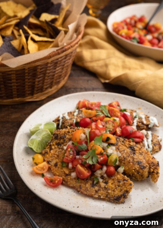 Crispy Tortilla Tilapia 2 Fried tortilla chip crusted tilapia fillets on an ivory plate with cherry tomato pico de gallo