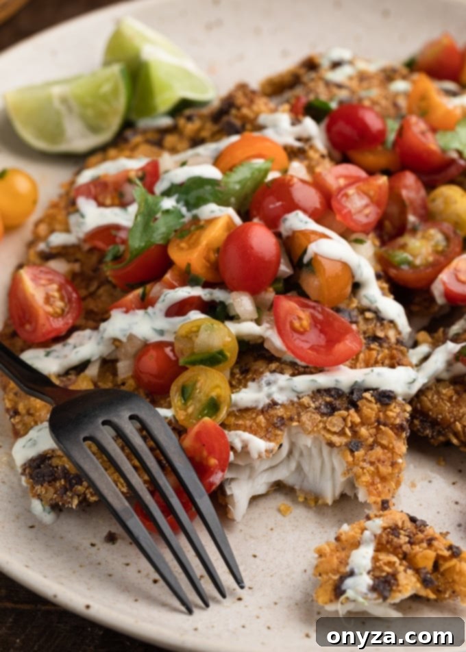 Crispy Tortilla Tilapia 7 Closeup of tortilla crusted tilapia with cherry tomato pico de galllo and cilantro lime sauce on a plate.