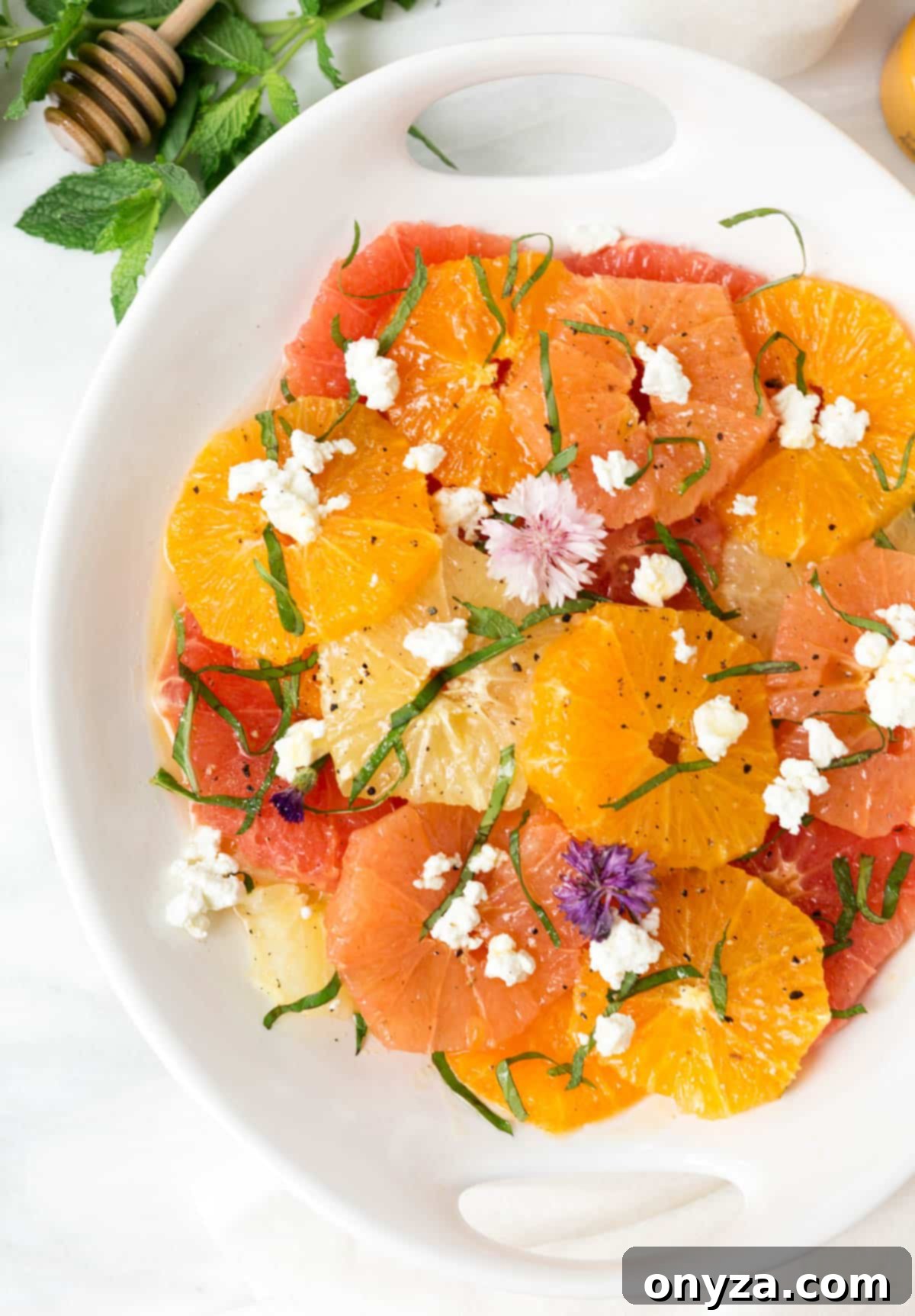 Vibrant citrus salad with crumbled goat cheese, fresh herbs, and edible flowers in a white serving dish