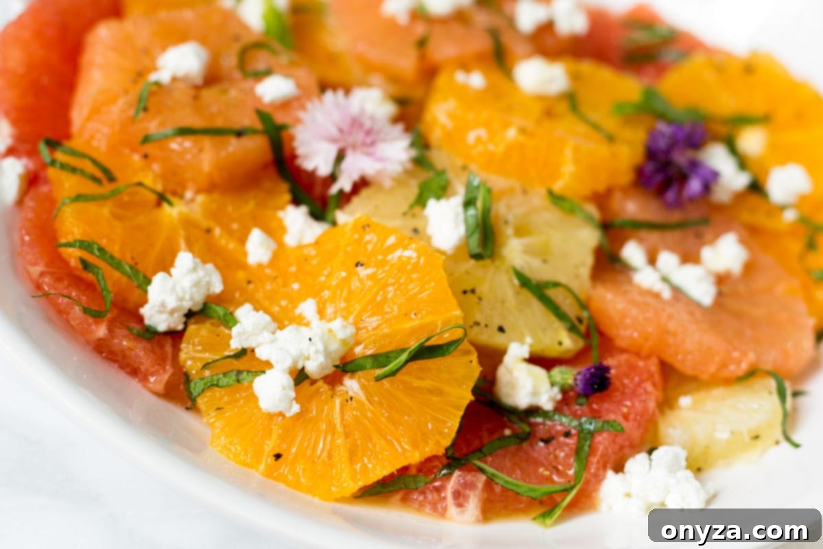 Close-up view of a vibrant citrus salad with goat cheese and herbs on a white platter