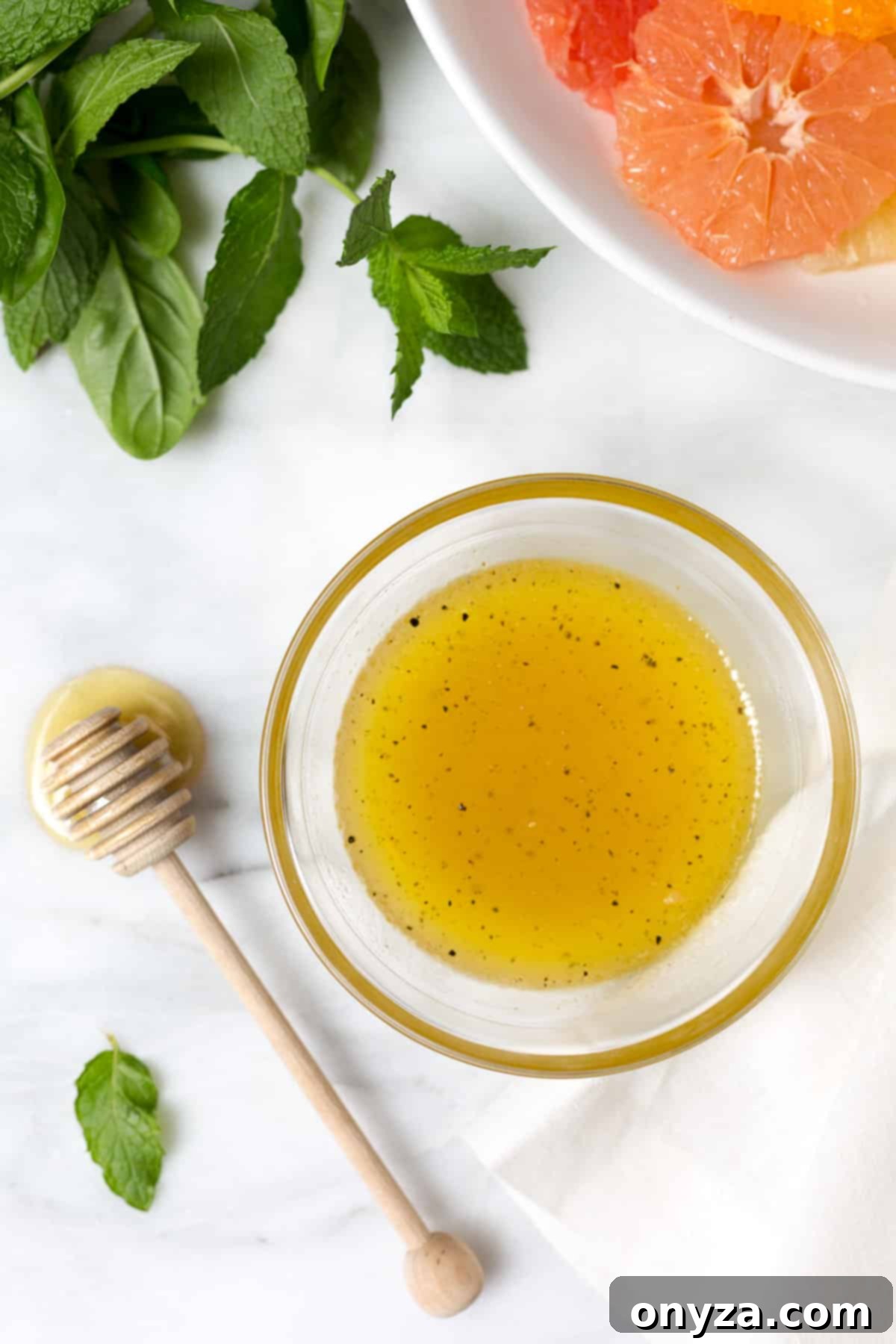 Overhead photo of honey balsamic vinaigrette in a glass bowl next to a honey dipper on a white marble board