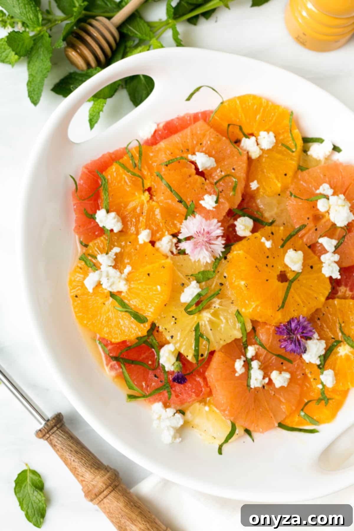 Mixed citrus salad with goat cheese and herbs in a white serving bowl on a white marble board