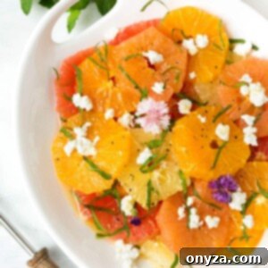Vibrant citrus salad with crumbled goat cheese, herbs, and edible flowers in a white serving dish