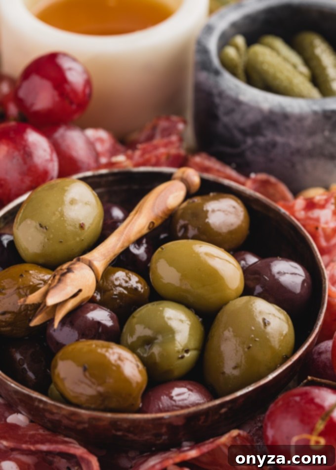 A vibrant cheese board close-up, showcasing a small bowl of olives, a drizzle of honey, and cornichons alongside beautifully arranged charcuterie, fresh fruit, and cheeses.