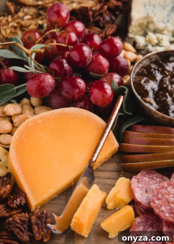 A beautifully composed cheese board featuring a large wedge of aged gouda, clusters of fresh grapes, sliced pears, an assortment of charcuterie, and various nuts, all invitingly arranged.