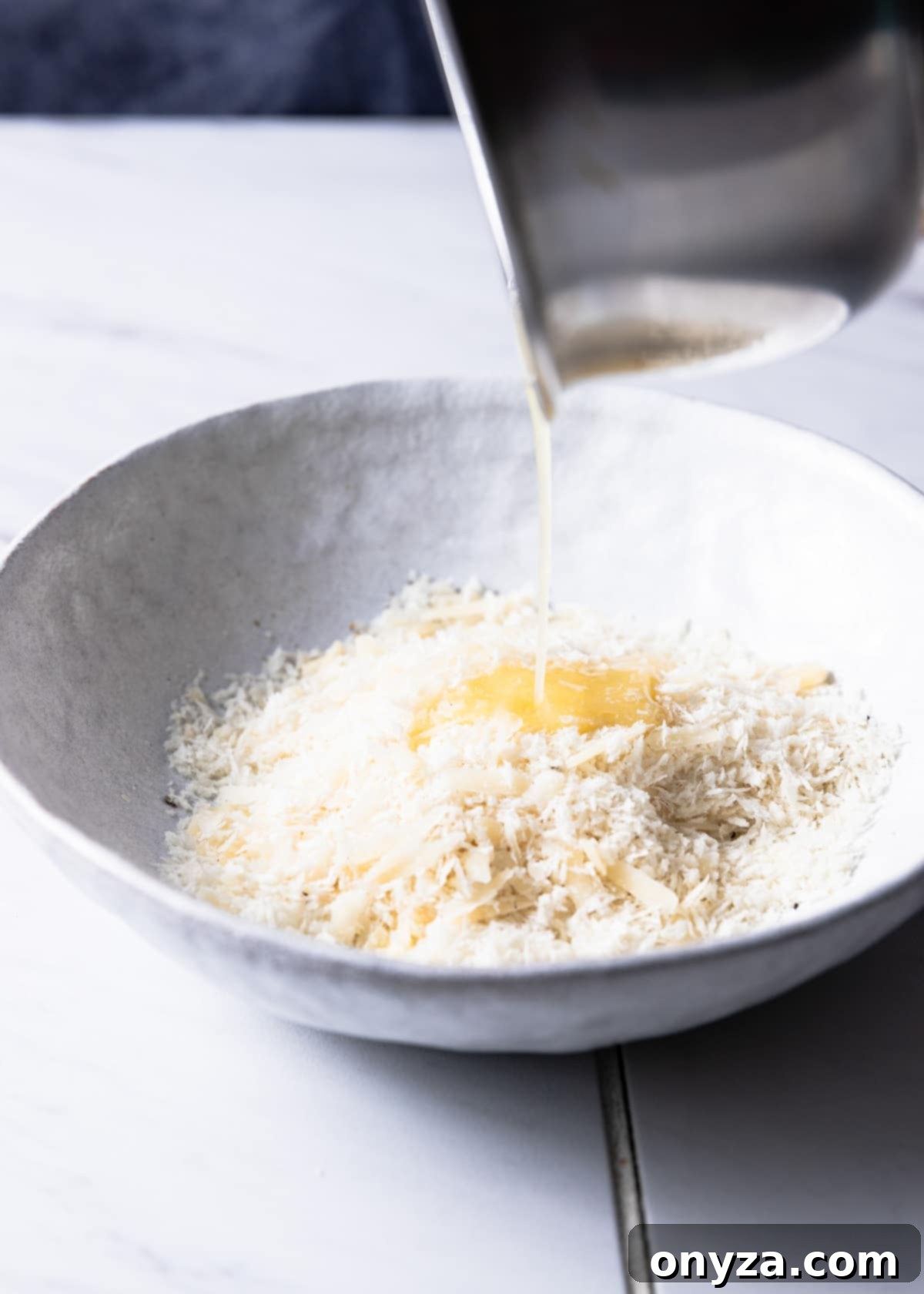 drizzlilng melted butter into a white bowl filled with panko breadcrumbs and parmesan cheese