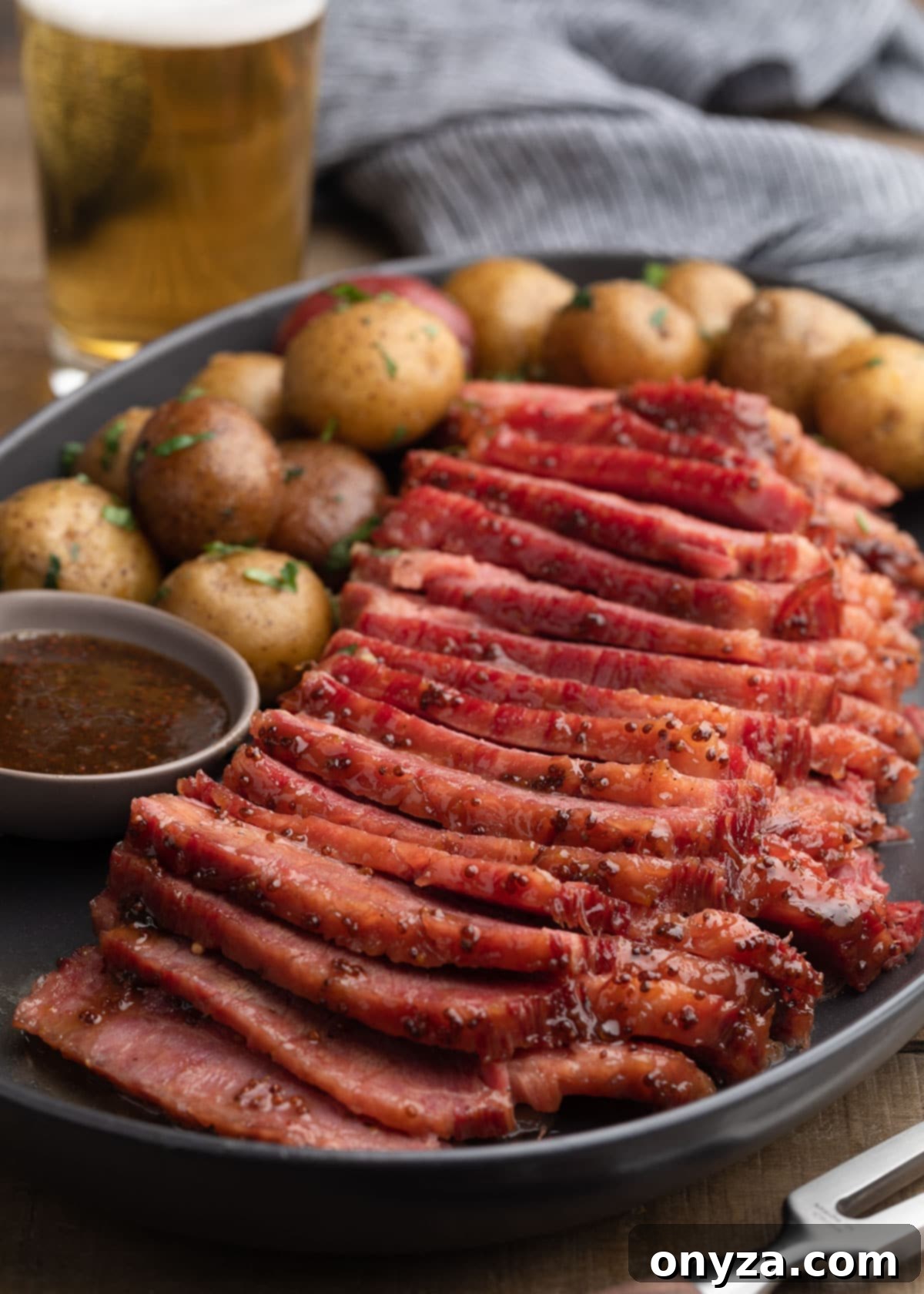 Golden Beer Braised Corned Beef Glazed with Whiskey Mustard 2 Sliced beer braised corned beef with whiskey mustard glaze on a gray ceramic platter with baby potatoes