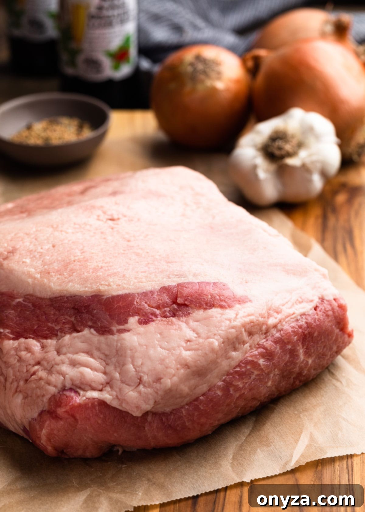 Golden Beer Braised Corned Beef Glazed with Whiskey Mustard 3 Uncooked corned beef brisket on a parchment lined wood cutting board with onions and garlic
