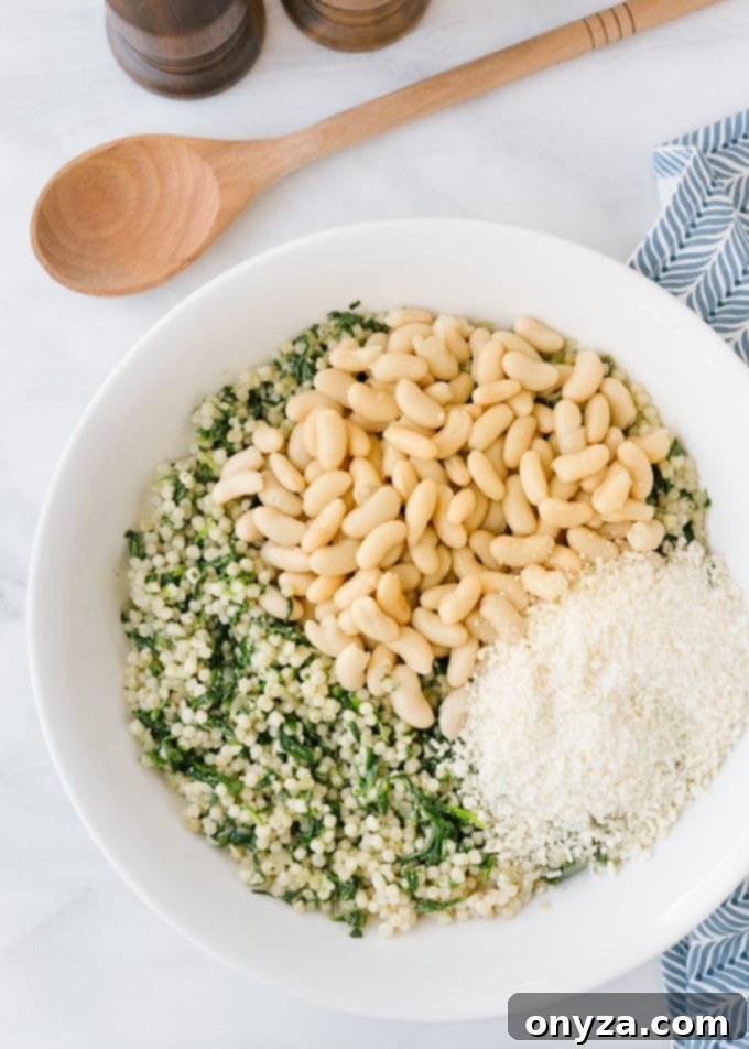 Close-up shot of pearled couscous being mixed in a white bowl with sauteed spinach, cannellini beans, and grated parmesan cheese, forming a delicious and healthy filling.