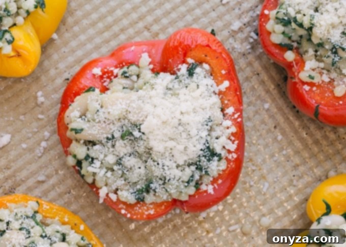 Overhead view of colorful unbaked vegetarian stuffed peppers filled with pearled couscous mixture, neatly arranged on a baking sheet, ready for the oven.