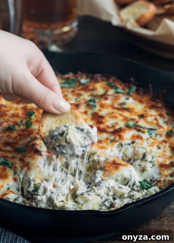 Golden, bubbly six-cheese spinach artichoke dip being scooped with a crostini