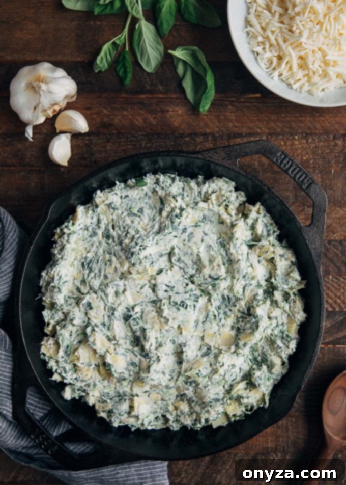 Unbaked six-cheese spinach artichoke dip prepared in a round cast iron skillet, ready for the oven