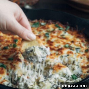 Golden, bubbly six-cheese spinach artichoke dip being scooped with a crostini, perfect for parties