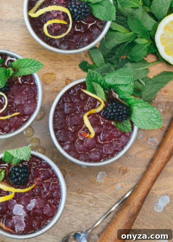 two summer cocktails: blackberry mint juleps served in julep cups on a wooden surface with fresh mint and berries