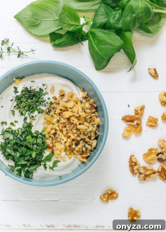 Adding the herbs and walnuts | Striped Spatula Whipped goat cheese being prepared with fresh herbs and walnuts, showing the ingredients mixing into a creamy texture.