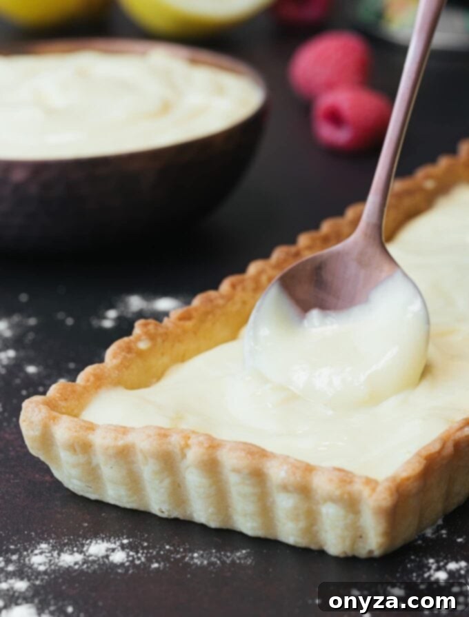 Lemon pastry cream being added to a golden tart shell