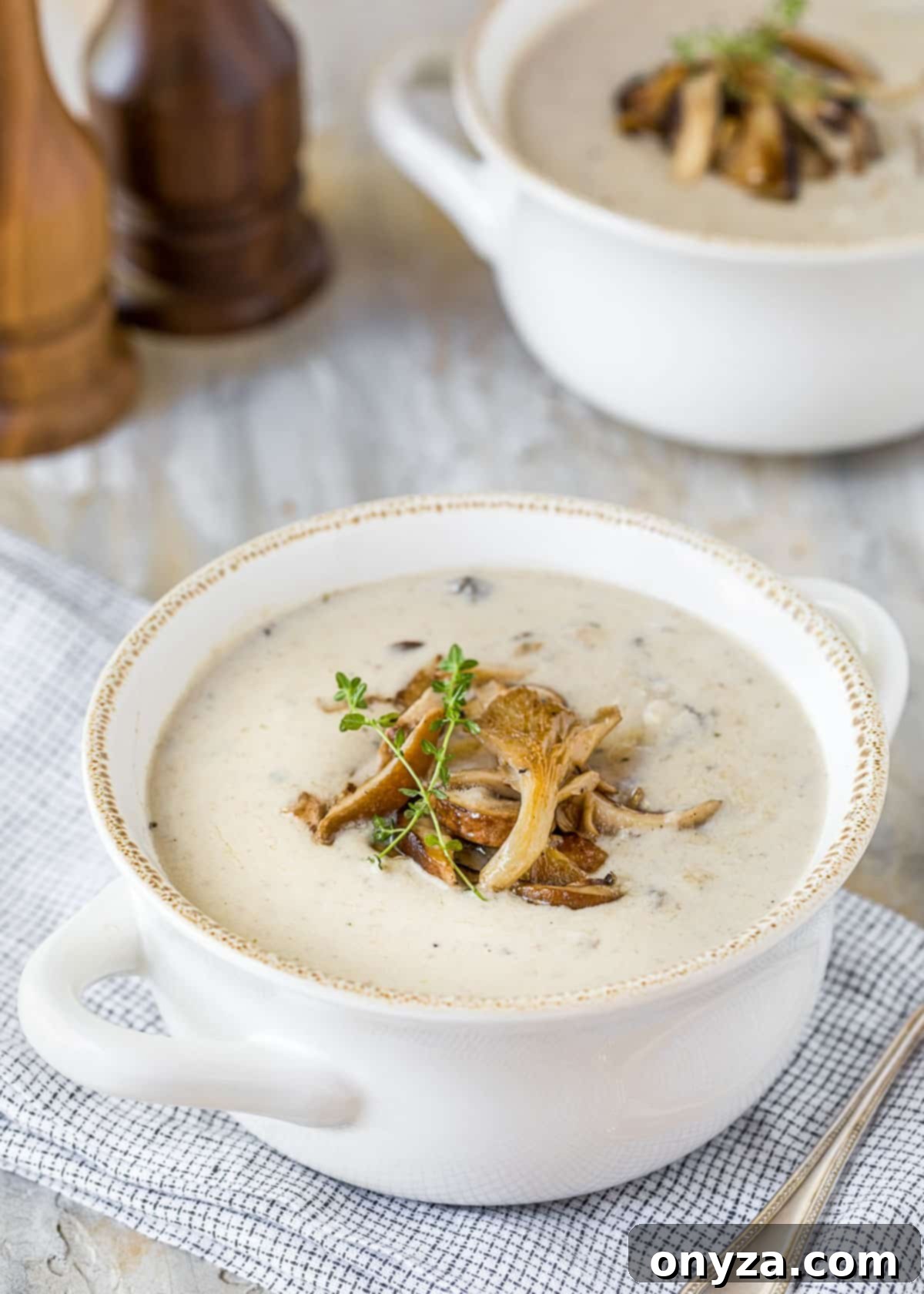 Two white handled bowls of rich homemade cream of mushroom soup garnished with sauteed mushrooms and fresh thyme sprigs, ready to serve.
