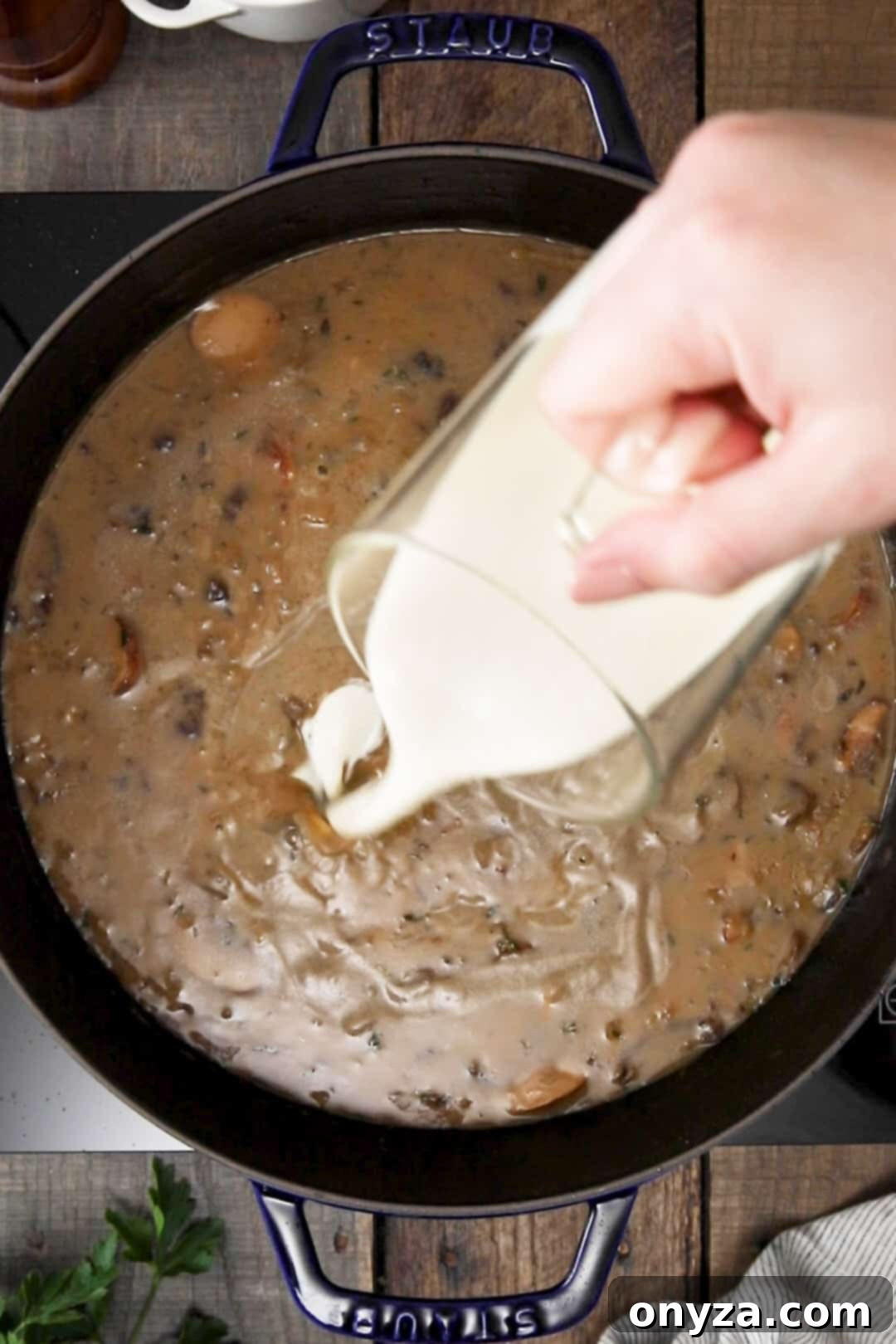 Heavy cream being poured from a glass measuring cup into a pot of homemade mushroom soup for a rich finish.