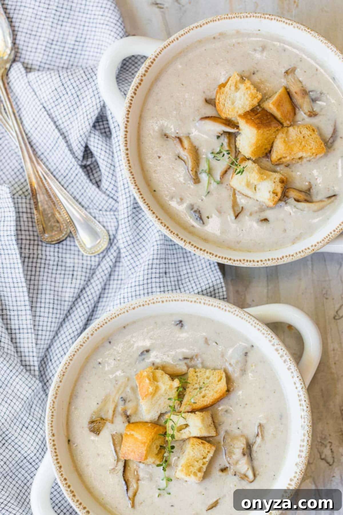 Overhead view of two elegant white double-handled soup bowls, each generously filled with homemade cream of mushroom soup and garnished with crispy homemade croutons, ready for a comforting meal.