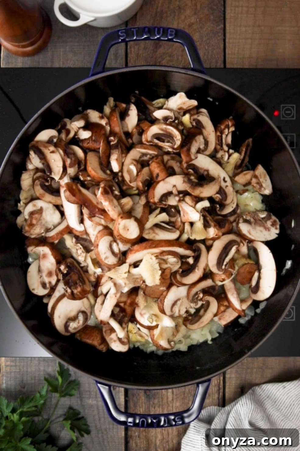 Sliced mixed mushrooms added to softened chopped onions in a black enameled cast iron Dutch oven.