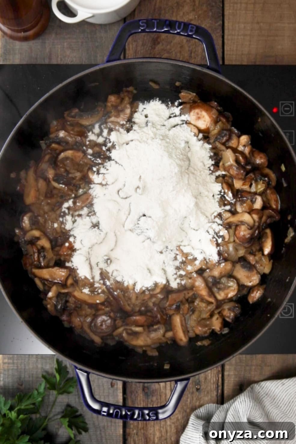 All-purpose flour evenly sprinkled over cooked mushrooms and onions in a black enameled cast iron Dutch oven, stirred to create a roux.